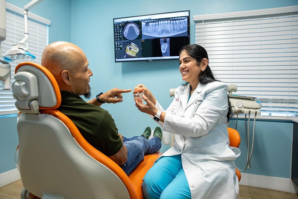 Dr. Uttma Dham talking with a patient in the treatment chair, scans on the screen